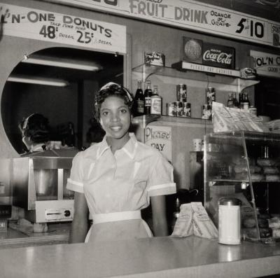Ernest C. Withers, A young African American woman wears a white blouse and apron and stands behind a diner counter.